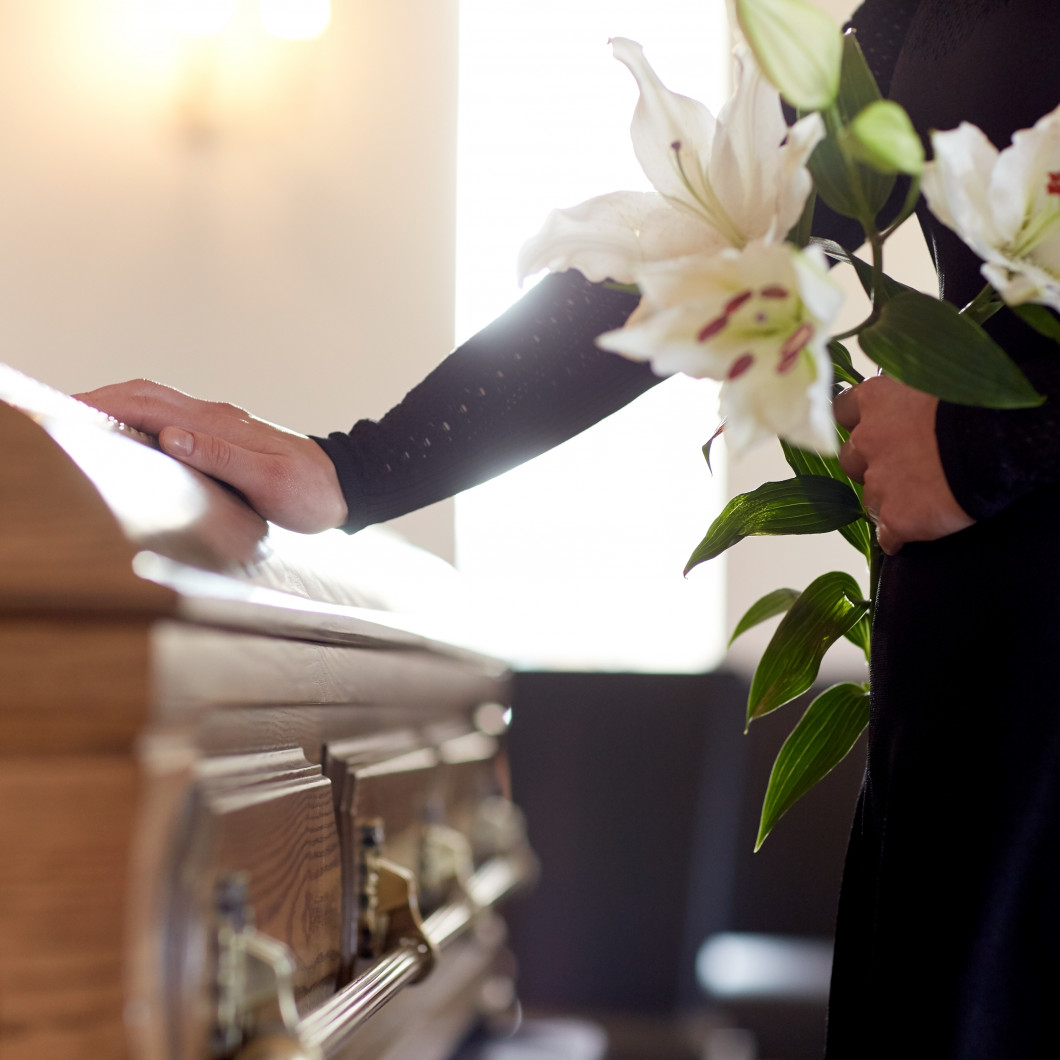 Woman placing her hand on casket while holding flowers